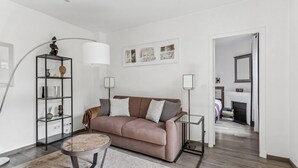A modern living room with a sofa, a round coffee table, a floor lamp, and a bookshelf. - Loft Fraternité (Bagnolet)