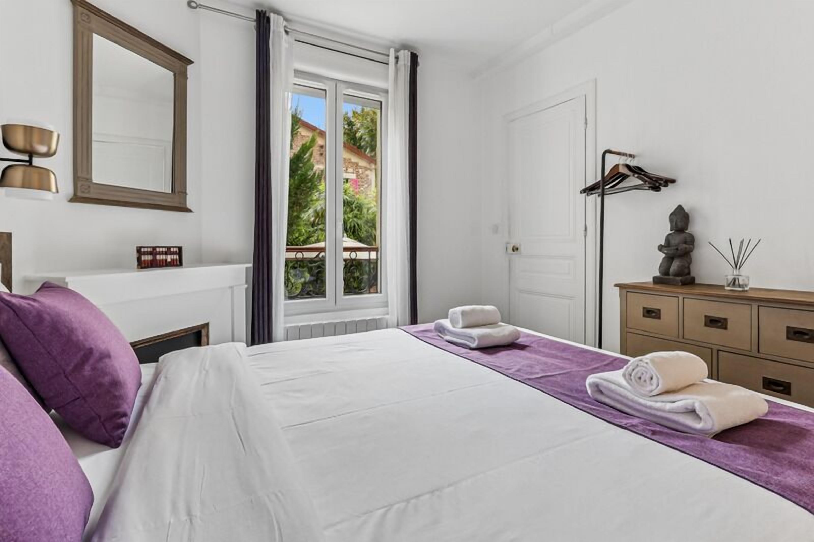 A hotel room with a bed, a dresser, a mirror, a window with curtains, and a statue.