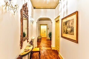 Un pasillo con suelo de madera, una mesa con un cojín amarillo, un espejo y un cuadro enmarcado en la pared.