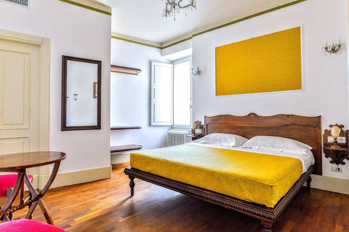 Un dormitorio con una cama de madera, una colcha amarilla, una puerta blanca, una ventana y una obra de arte amarilla en la pared.