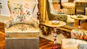 A room with a floral-patterned armchair, a matching armchair, a round table with a plate, and a mirror with a gold frame. - Arpinelli Relais (Rome)