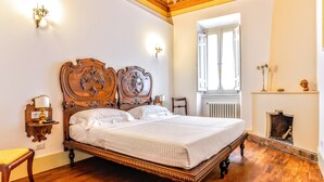 A spacious bedroom with a large wooden bed, a chair, and a nightstand with a lamp. - Arpinelli Relais (Rome)