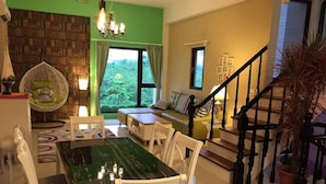A dining area with a green table and white chairs, a staircase with black railings, and a view of greenery outside. - Riverstupid B&B (Hengchun)