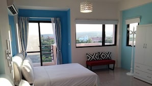A hotel room with two beds, a bench, a wardrobe, and large windows offering a view of the city. - Riverstupid B&B (Hengchun)