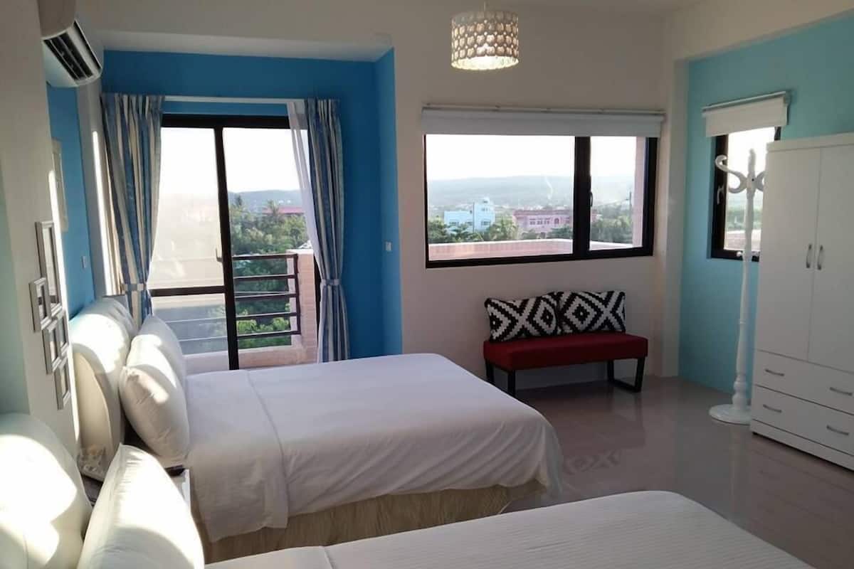 Habitación de hotel con dos camas, un banco, un armario y ventanas amplias con vistas a la ciudad.