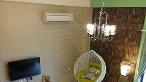 A modern living room with a flat-screen TV, a white entertainment unit, a patterned rug, a wooden coffee table, a green cushioned chair, and a bookshelf. - Riverstupid B&B (Hengchun)