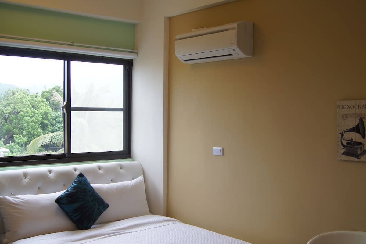 Un dormitorio con cama, ventana, aire acondicionado y una silla.