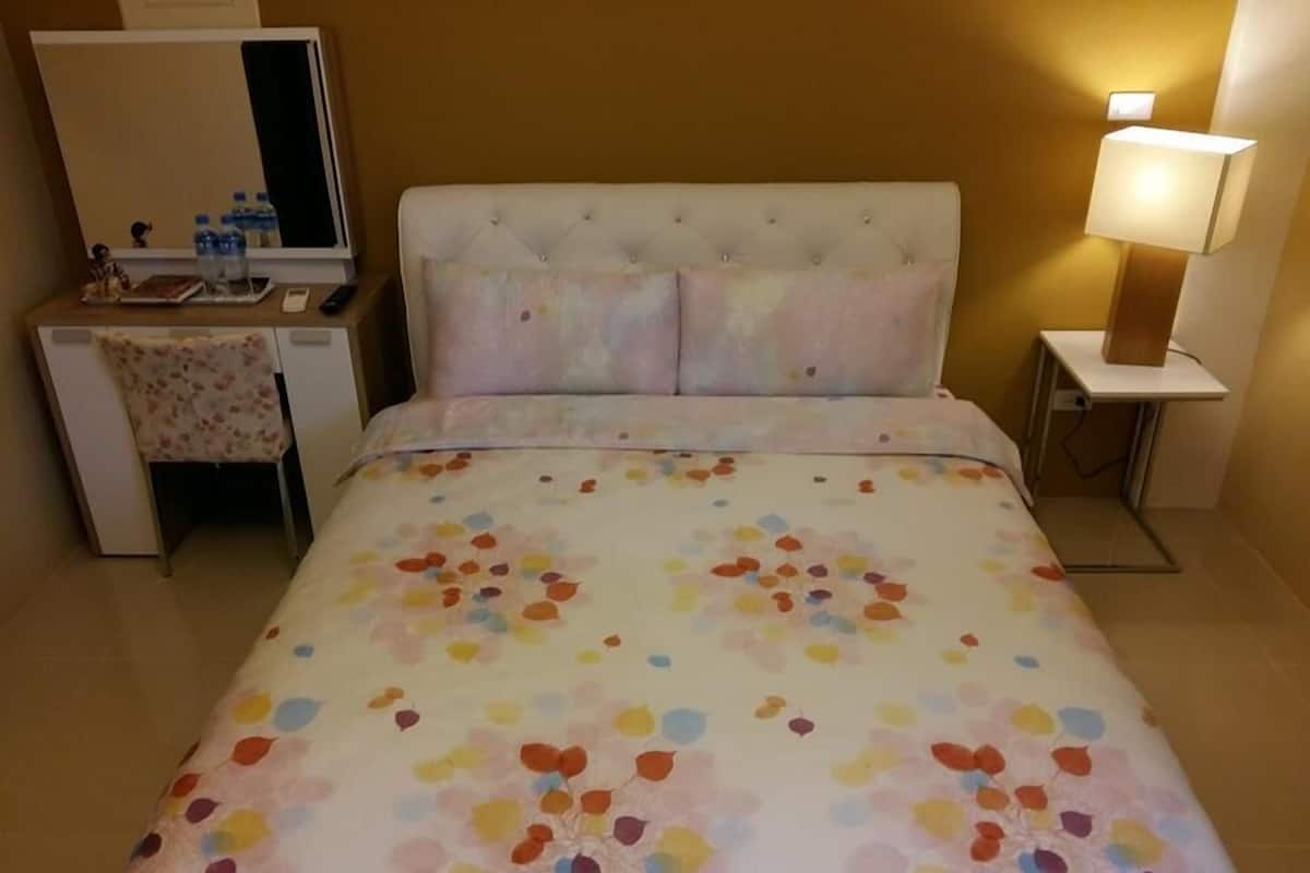Una habitación de hotel con cama, escritorio, silla, espejo y lámpara de noche.
