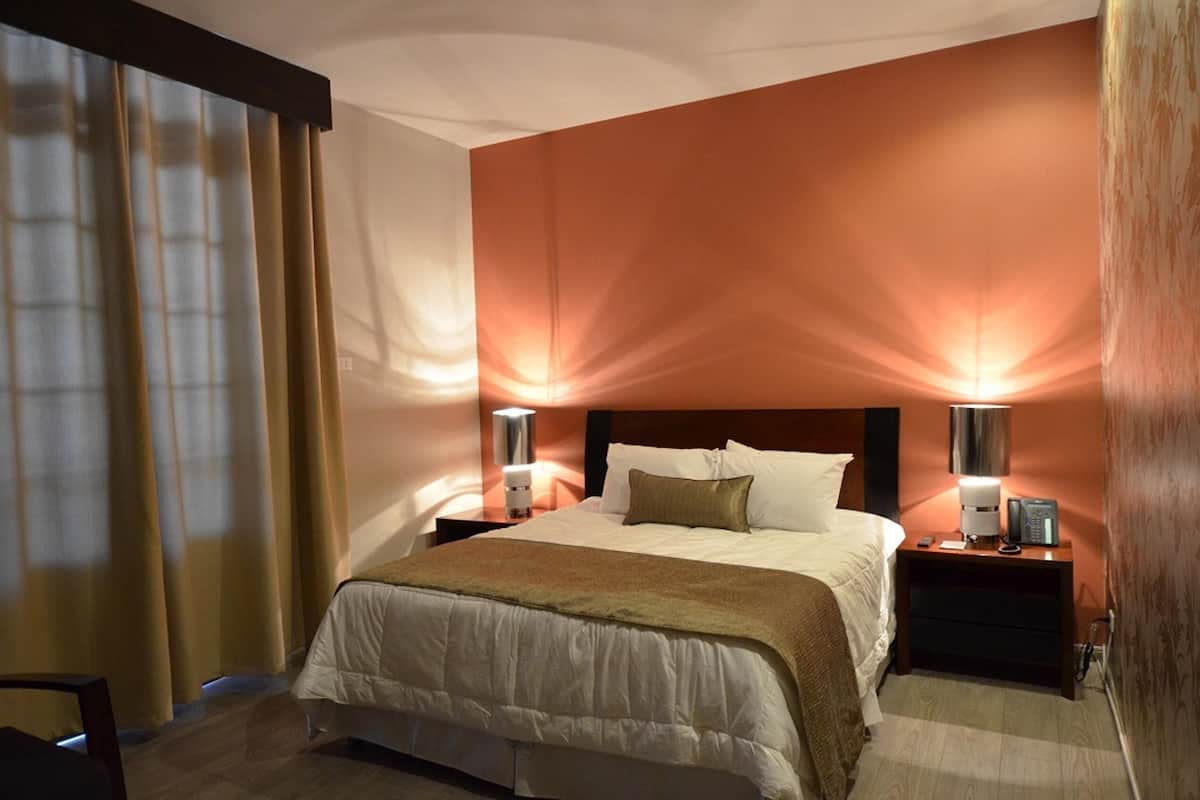 Een hotelkamer met een bed, twee bedlampen, een nachtkastje en een stoel.