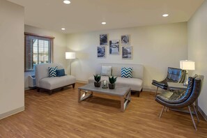 A living room with a sofa, armchair, coffee table, and a lamp. - WoodSpring Suites Frederick I-70 (Frederick)