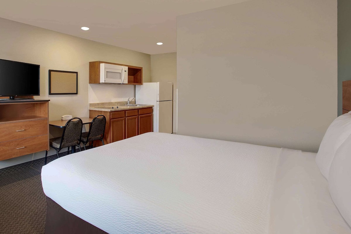 A hotel room with a large bed, a desk with a chair, a microwave, a refrigerator, and a television.