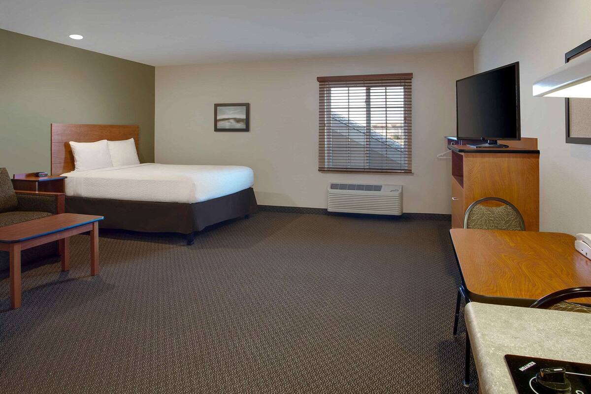 A hotel room with a bed, a desk, a chair, a TV, and a window with blinds.