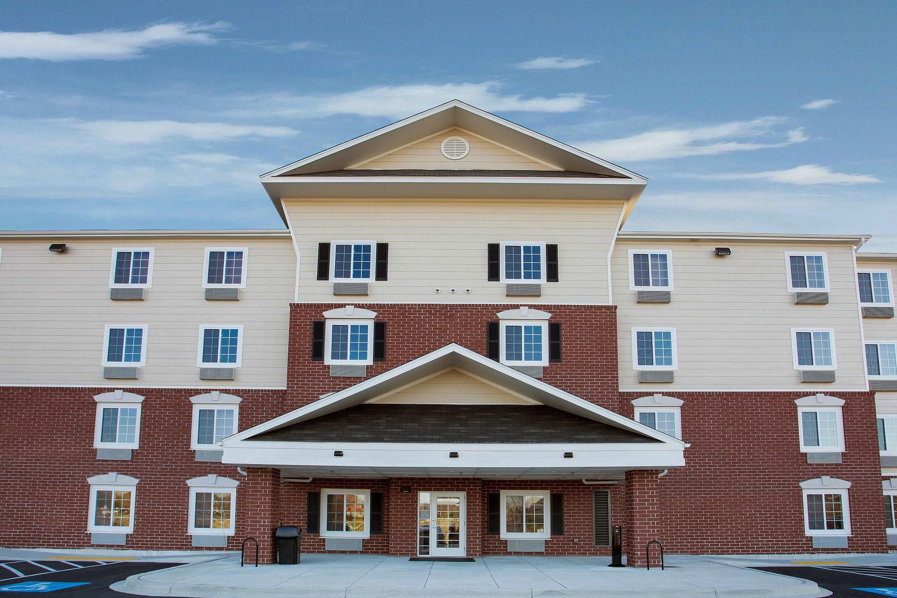 A multi-story building with a symmetrical facade, featuring a central entrance with a triangular pediment, multiple windows with shutters, and a brick lower section.