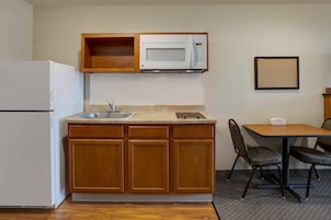 Una kitchenette compacta con microondas, lavamanos y un pequeño comedor con mesa y sillas.