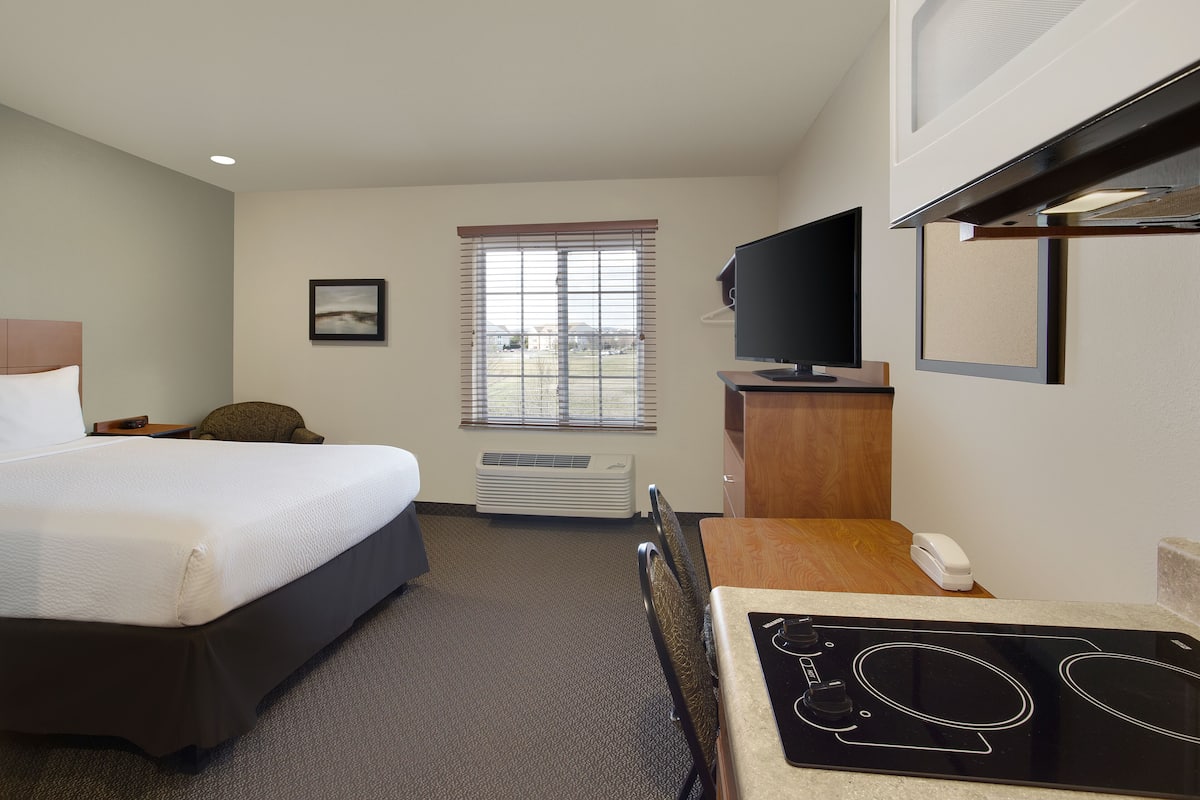 A hotel room with a bed, a desk with a telephone, a television, and a window with blinds.