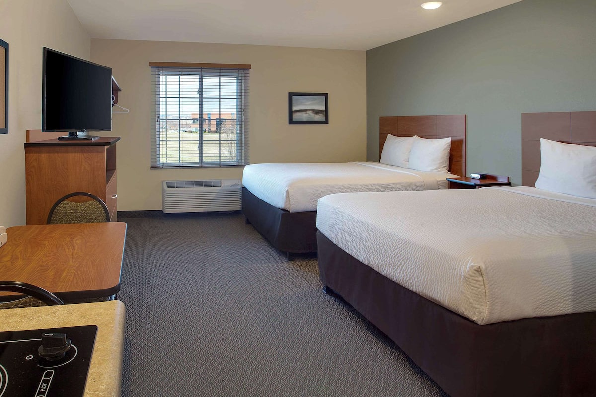 A hotel room with two beds, a desk, a television, and a window with blinds.
