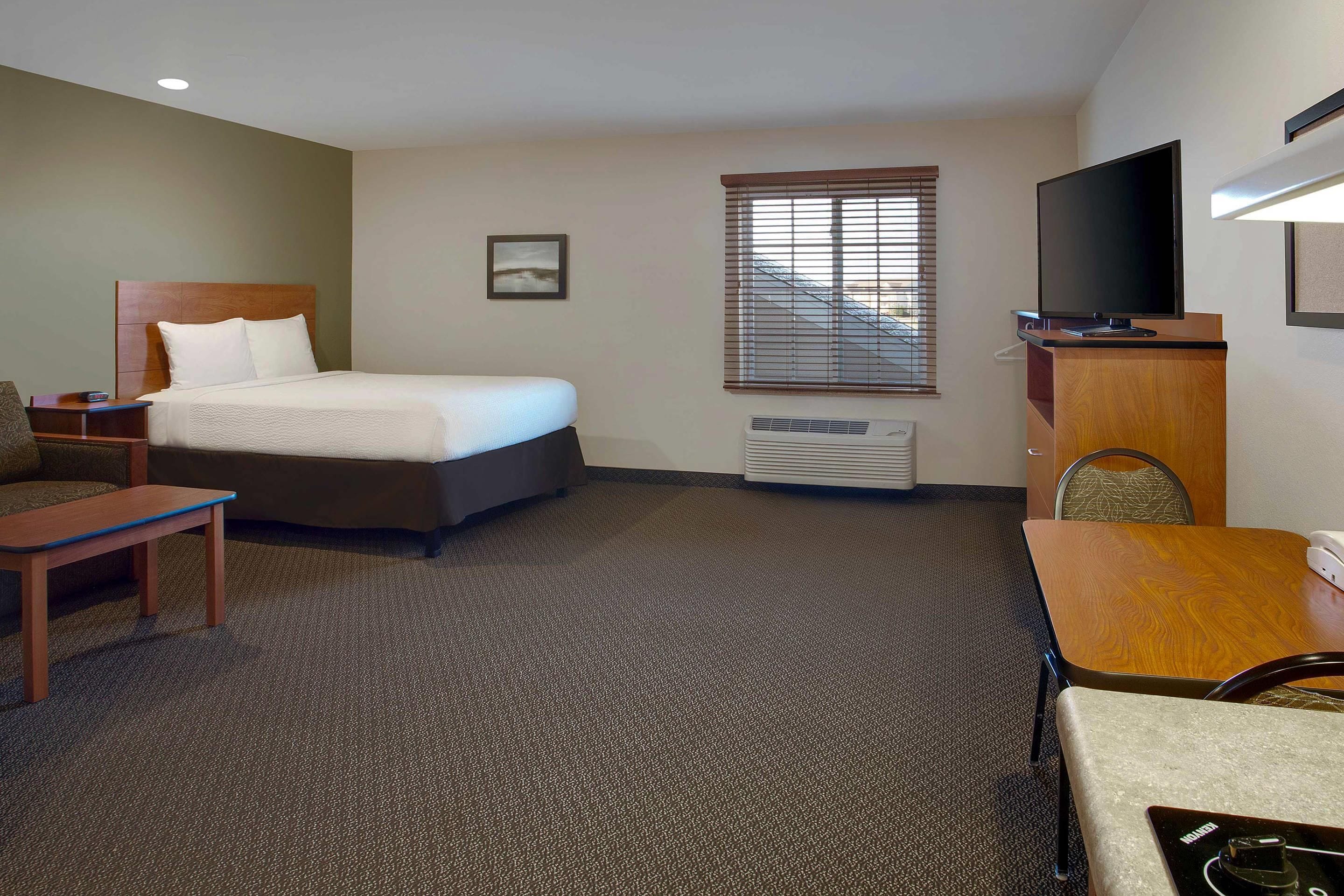 A hotel room with a bed, a desk, a chair, a television, and a window with blinds.