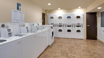 A laundry facility with multiple washing machines and dryers, a sign with laundry instructions, and a door to the right.