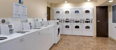 A laundry facility with multiple washing machines and dryers, a sign with laundry instructions, and a door to the right.