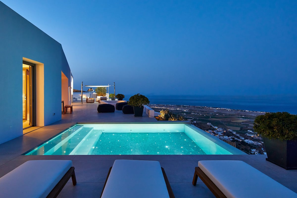 A modern outdoor pool area with a view of the ocean at dusk, featuring a seating area with lounge chairs and a small table.