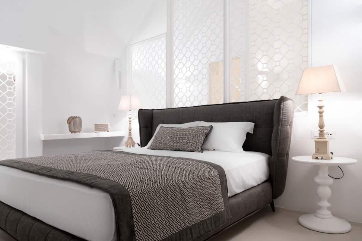 A modern bedroom with a large bed, a bedside table with a lamp, and decorative items on a shelf.