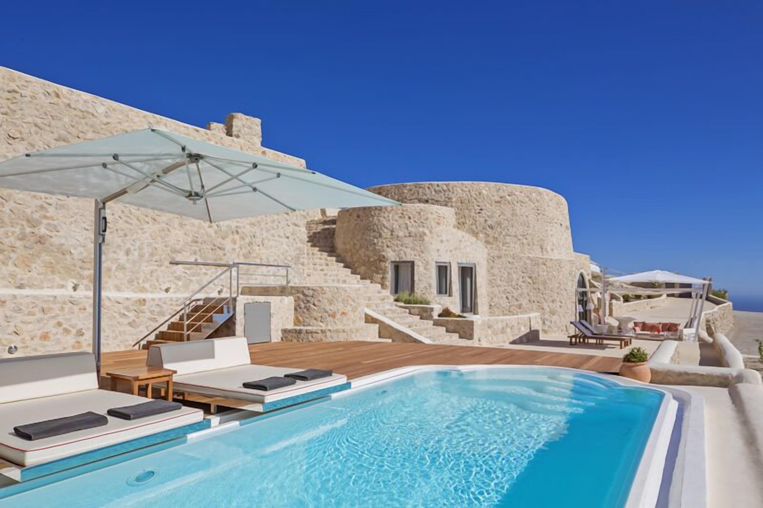 A pool area with a stone wall, a staircase, and a lounge with a table and chairs.