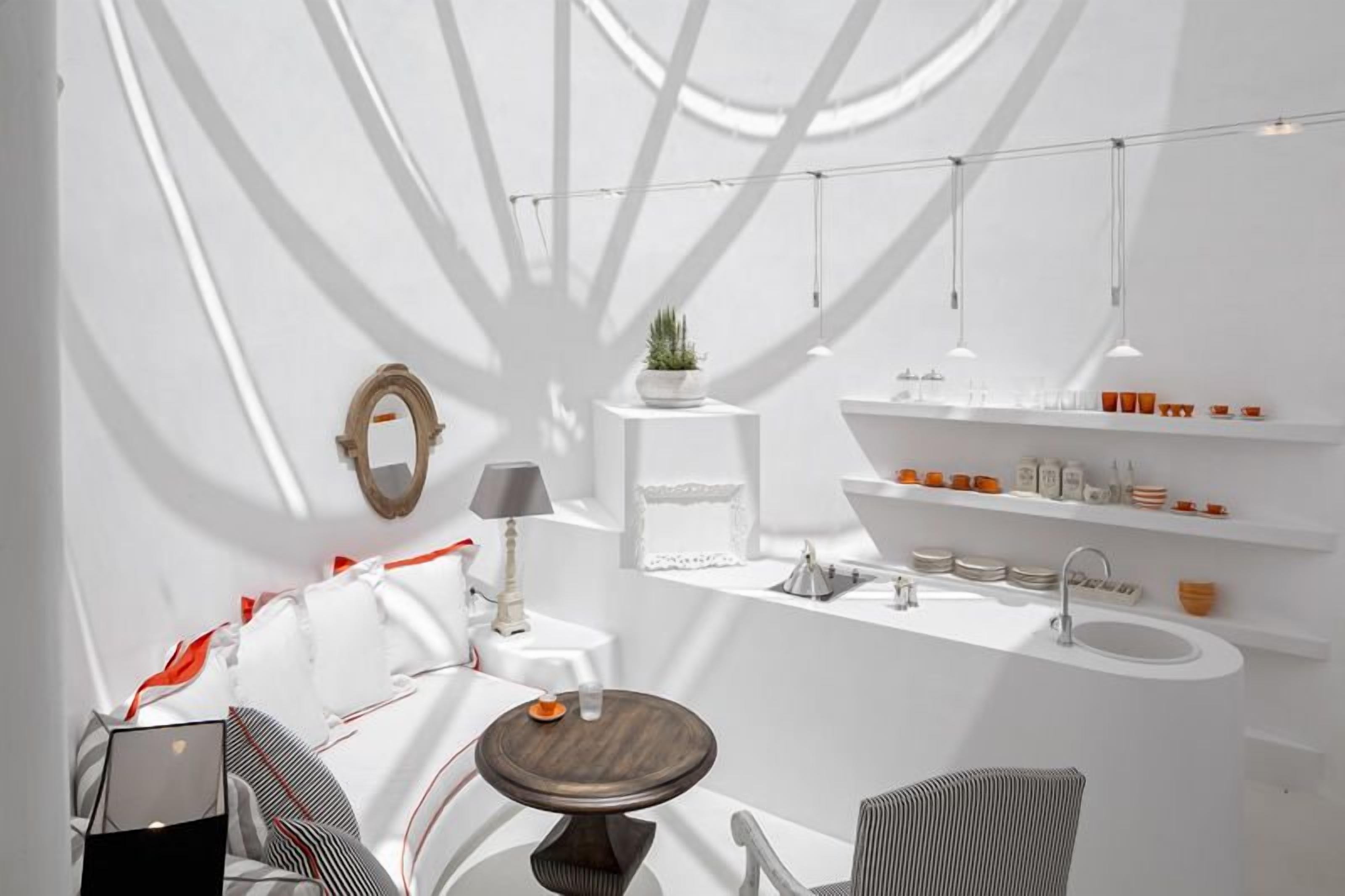 A modern bathroom with a white color scheme, a round wooden table, a small potted plant, and a shelf with toiletries.