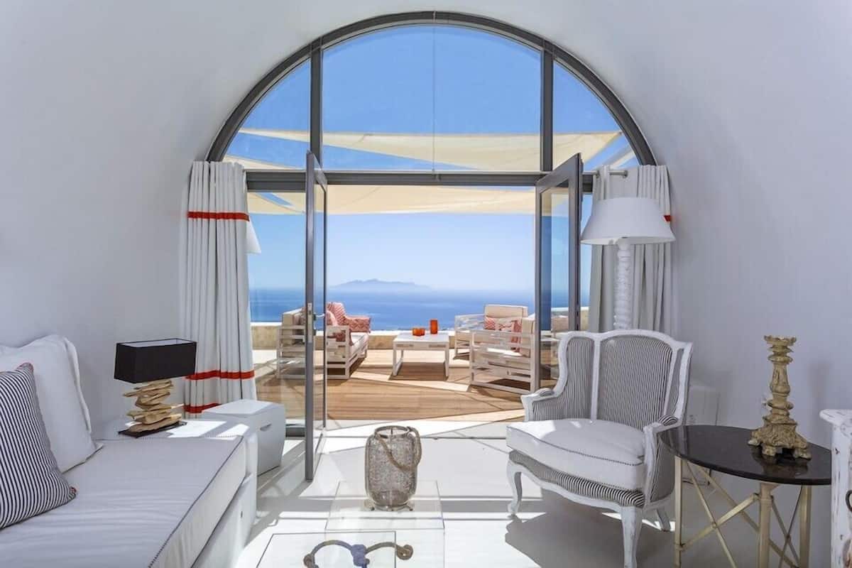 A modern hotel room with a large arched window offering a view of the sea.