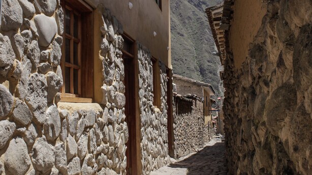 Une rue étroite, pavée de pierres, bordée de bâtiments traditionnels en pierre, dotés de portes et de fenêtres en bois.
