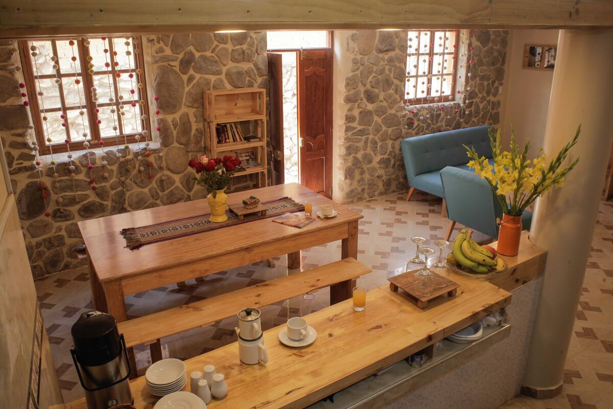 A cozy room with a wooden table, benches, a blue sofa, and a stone wall.