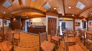 A spacious dining area with wooden tables and chairs, a central bar area, and walls adorned with framed pictures. - Thunderbird Lodge (Chinle)