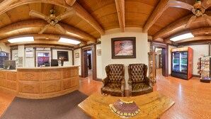 A lobby with wooden ceiling beams, a reception desk, leather armchairs, a Coca-Cola refrigerator, and a scenic view poster. - Thunderbird Lodge (Chinle)