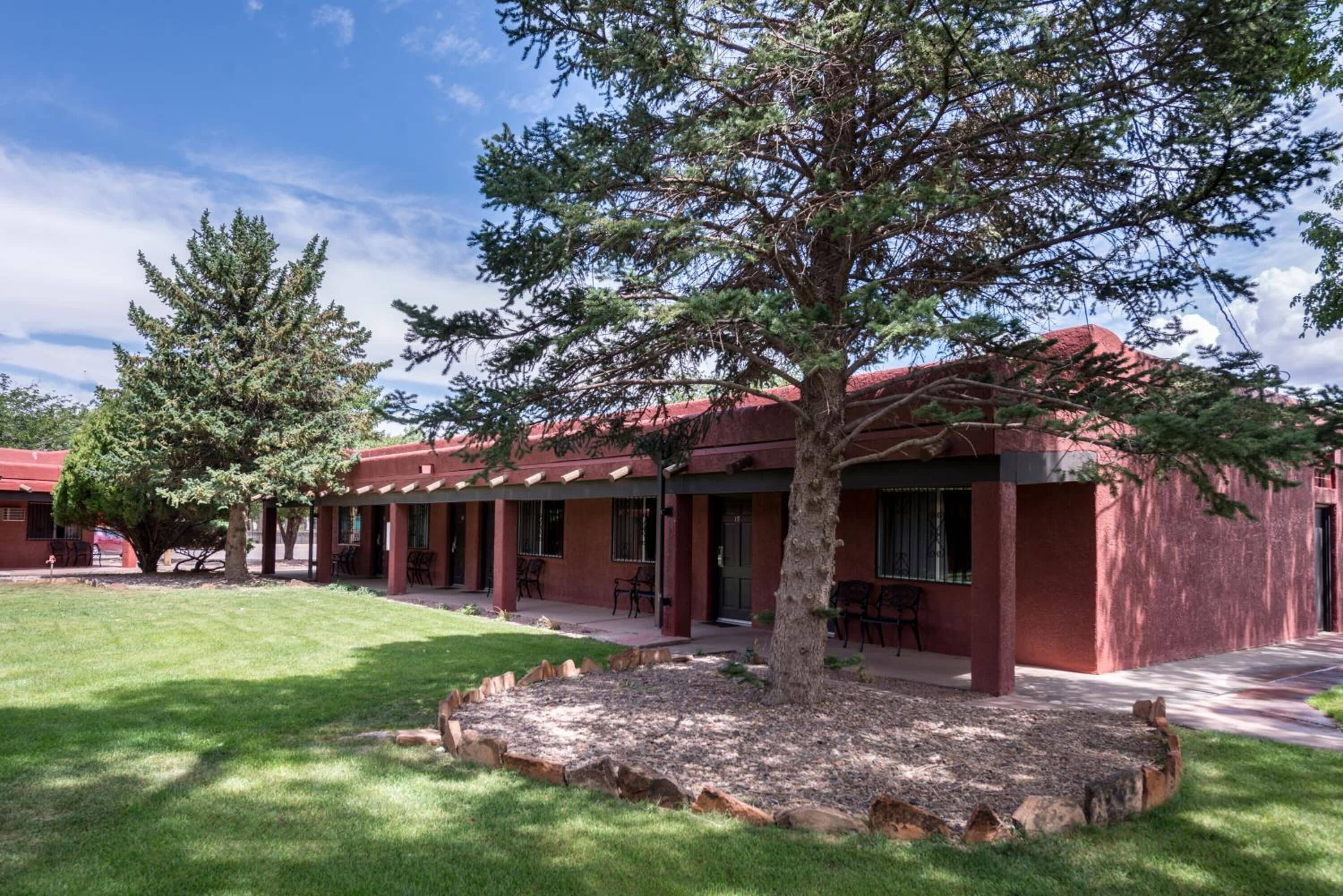 Un edificio de fachada roja, un patio cubierto con mobiliario exterior y un césped bien cuidado.