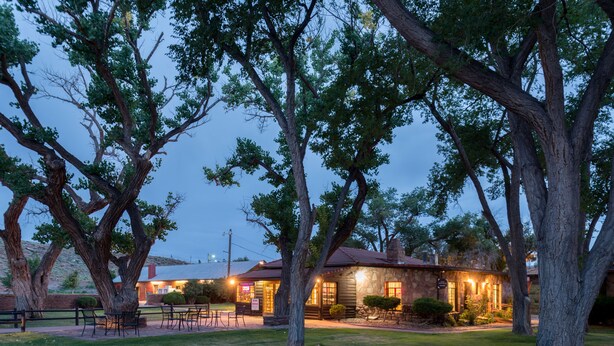 A rustic lodge with a stone facade, surrounded by large trees and a well-maintained lawn. - Thunderbird Lodge (Chinle)