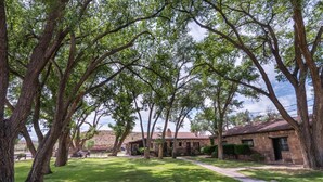A stone building with a red roof, surrounded by a well-maintained lawn and large trees. - Thunderbird Lodge (Chinle)