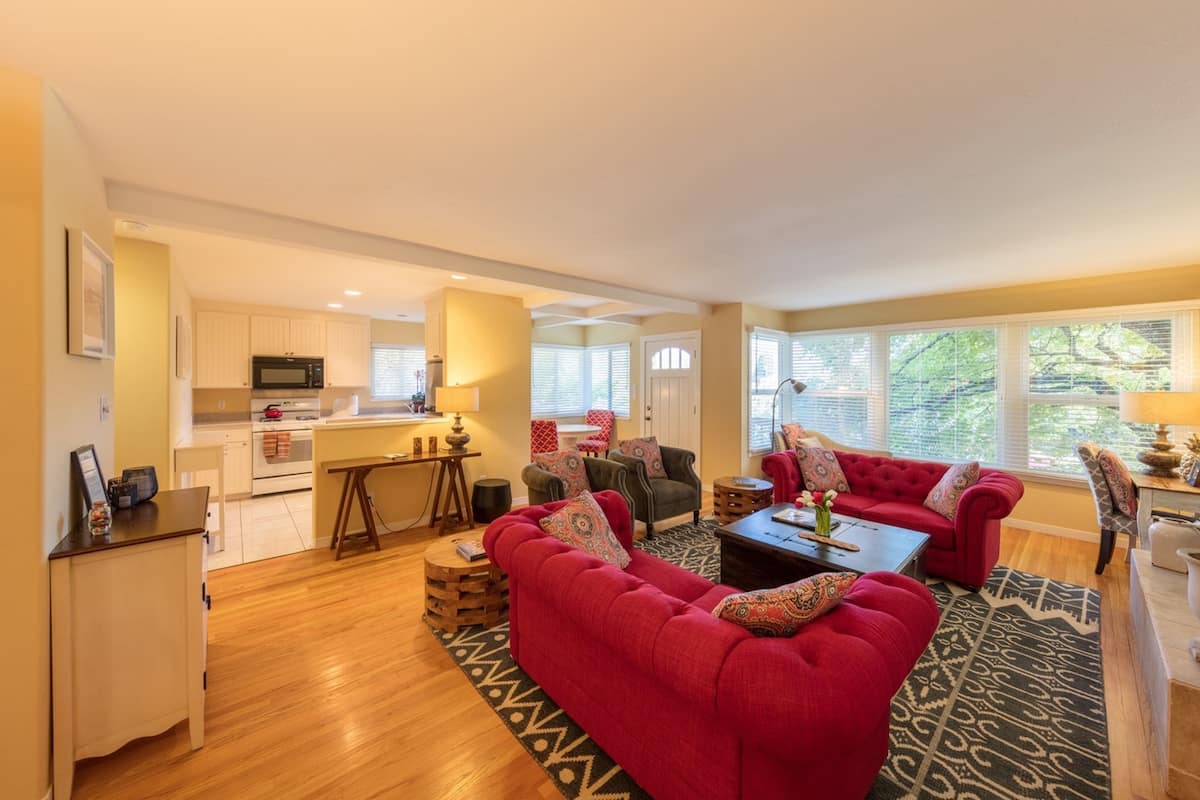 A spacious living room with a red sofa, a coffee table, and a dining area with a lamp.