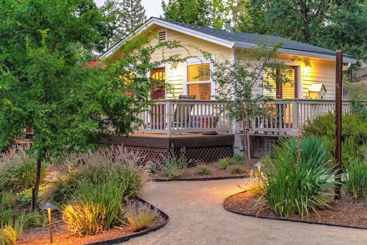 A house with a porch, surrounded by various plants and a pathway.