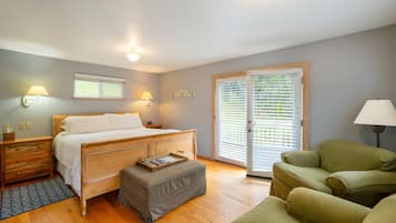 A bedroom with a wooden bed, a nightstand, a reading light, a window with blinds, and a green armchair.