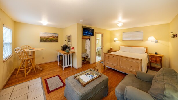A cozy room with a bed, a sofa, a dining table with chairs, a small kitchenette, and a bathroom. - Aurora Park Cottages (Calistoga)