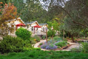 A row of wooden cabins with red umbrellas, surrounded by lush greenery and a winding path. - Aurora Park Cottages (Calistoga)