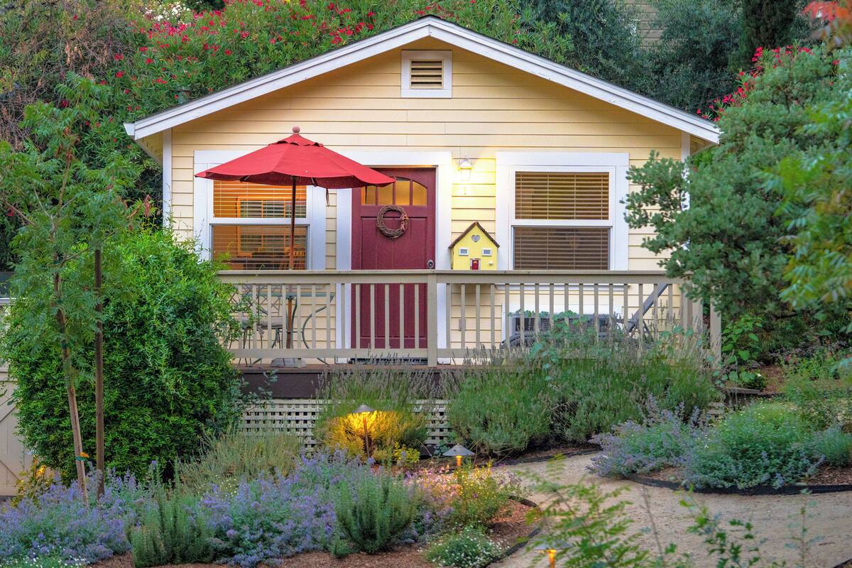 A house with a front porch, a red umbrella, and a garden with various plants.