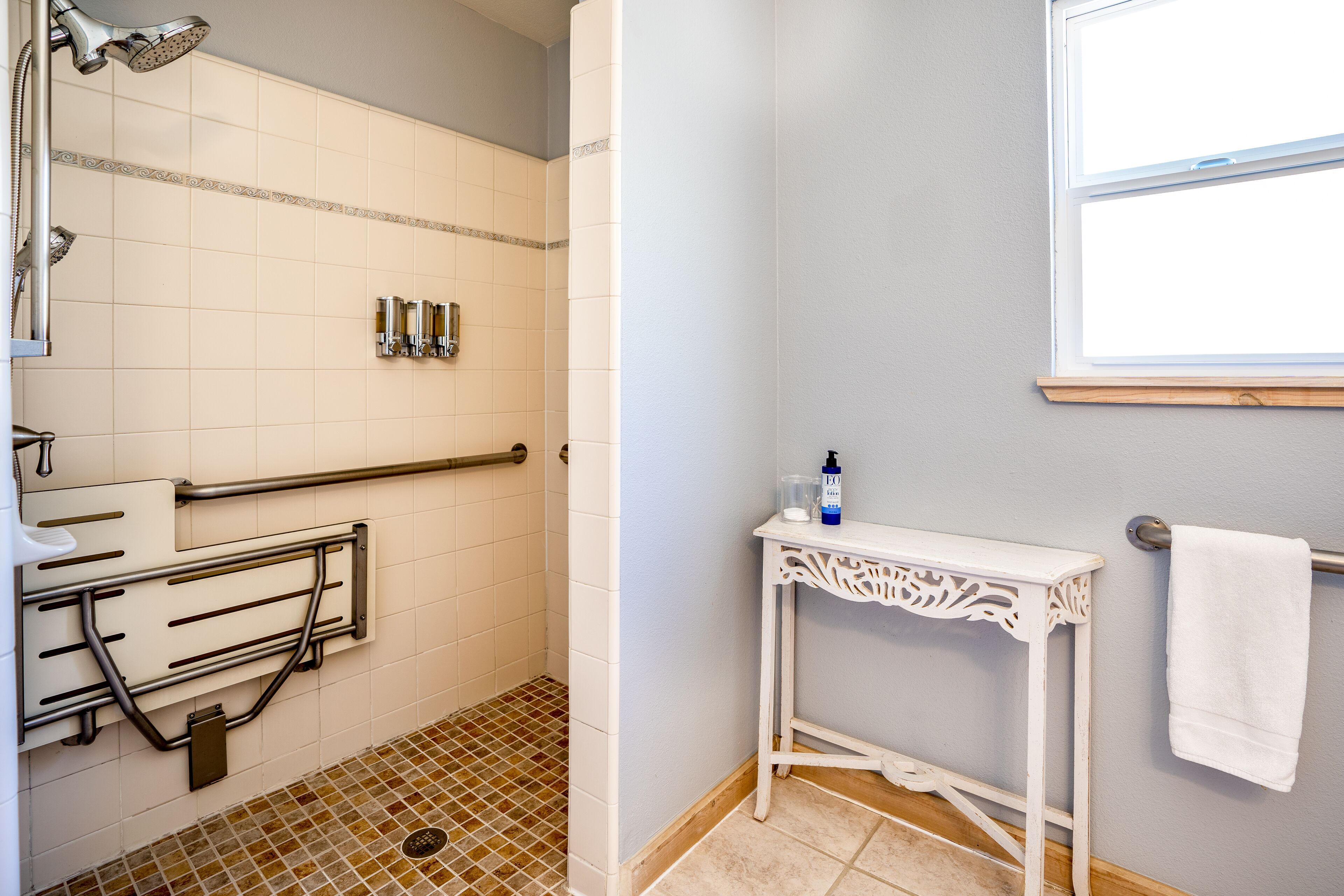 Een badkamer met douche, grepen, een witte wastafel en een raam.