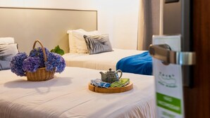 A hotel room with two beds, a basket of flowers, a tray with a teapot and magazines, and a door with a sign. - Hotel São Miguel (Ponta Delgada)