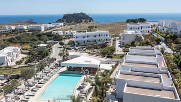 A resort with a swimming pool, white buildings, and a view of the sea.