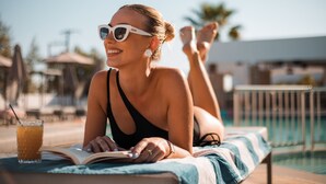 A person lying on a lounge chair by a pool with a book and a drink. - Lambis Studios & Apartments (Rhodes)