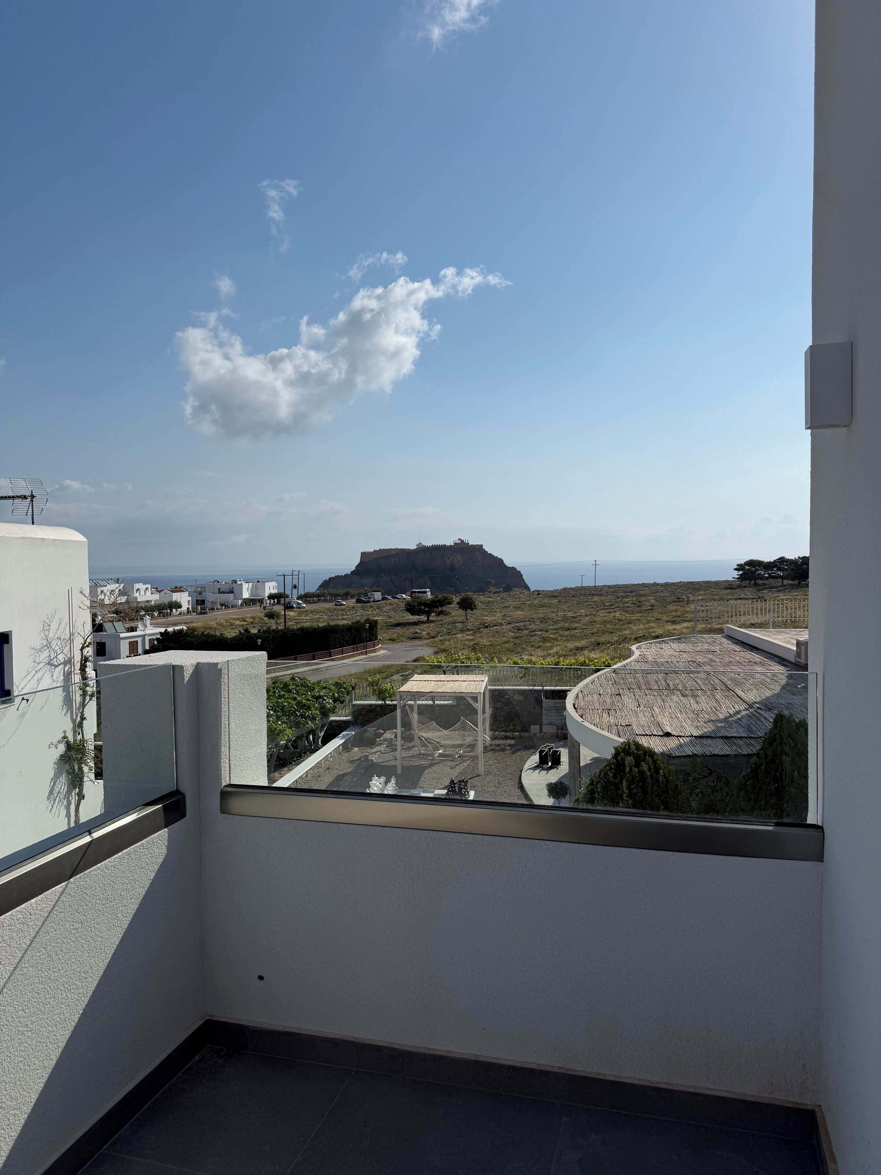 A balcony with a view of a hill and a building in the distance.