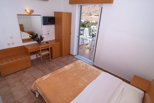 A bedroom with a bed, a desk, a chair, a mirror, and a balcony with a table and chairs. - Lambis Studios & Apartments (Rhodes)