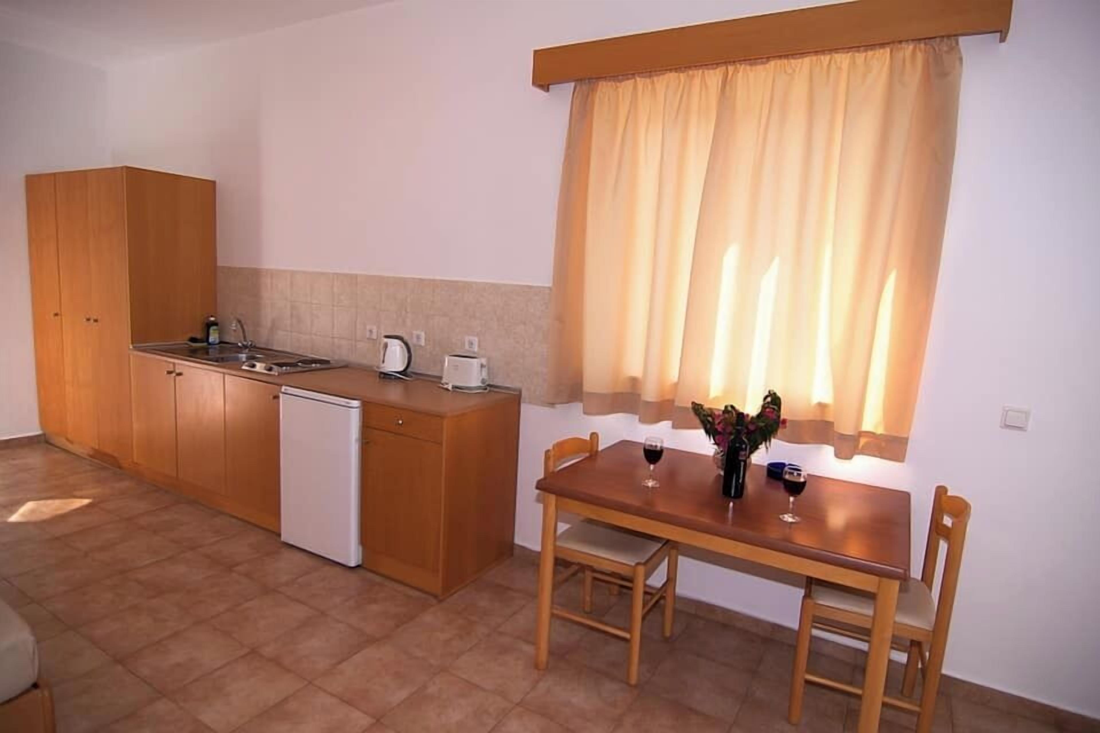A compact kitchen with a dining area, wooden cabinets, a white refrigerator, and a window with curtains.