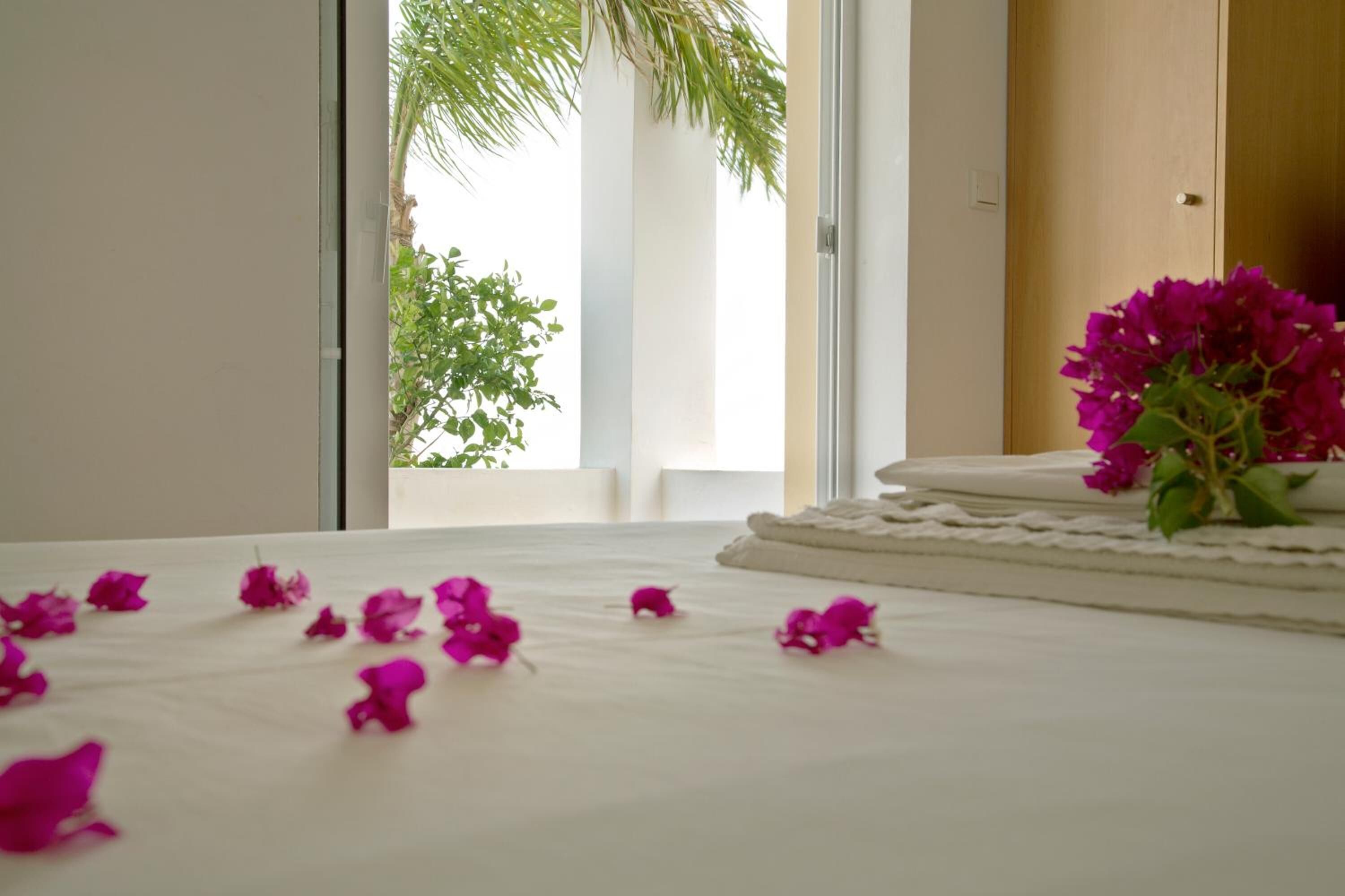 Habitación de hotel con cama, ventana con vista a follaje y un florero con flores sobre la cama.