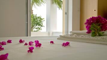 Habitación de hotel con cama, ventana con vista a follaje y un florero con flores sobre la cama.